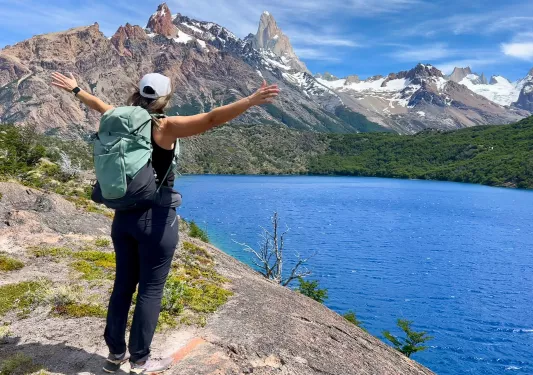 A person holds their arms wide open to a blue lake