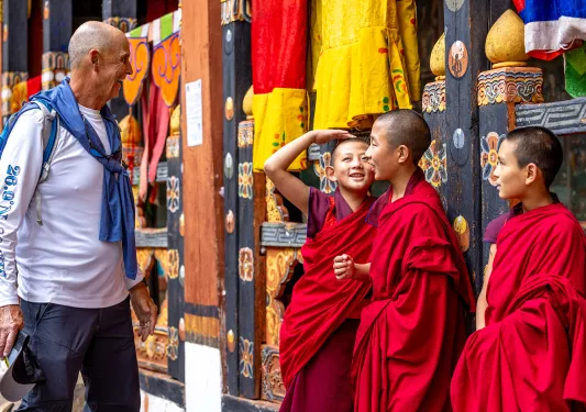 Man smiling and looking at 3 monk children in robes