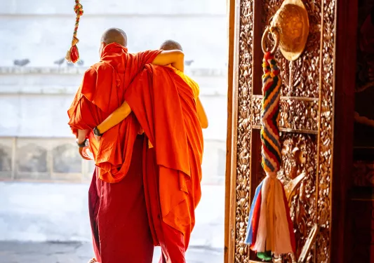 Two monks wearing orange robes in the doorway of a large temple
