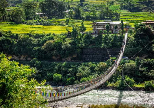 Group of hikers walking on a long, wooden bridge that is covered in colorful flags