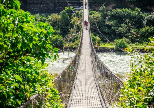 Groups of people walking on a long, wooden bridge over a river