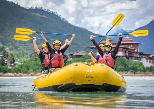 Group of people on a yellow raft, holding up their paddles