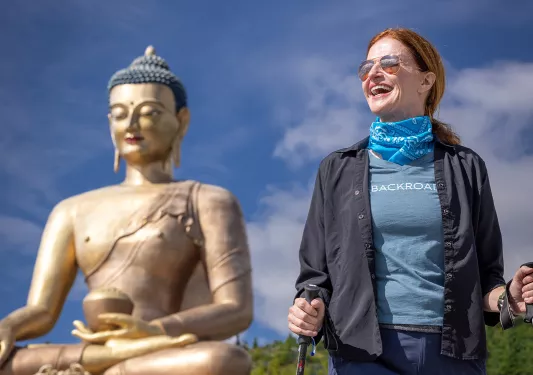 Woman walking in front of a giant temple with a Buddhist statue in the background