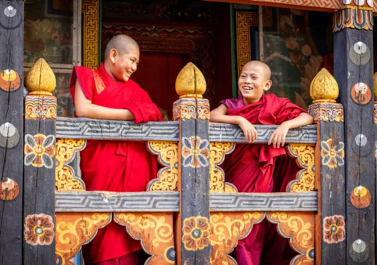 Two monk boys smiling while leaning on a wooden fence