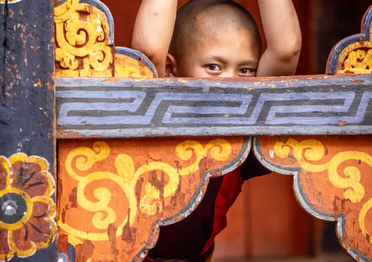 Monk child in a robe holding onto a wooden fence