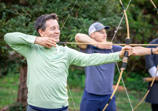 Two men smiling while holding up a bow and arrow