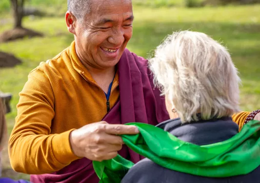 Monk wearing a robe putting a green scarf over a woman