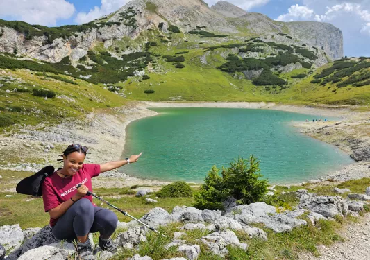 Woman sitting down and smiling, pointing at a small lake