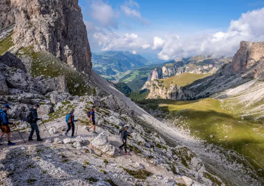 Group of people hiking down a rocky path next to a large valley of mountains