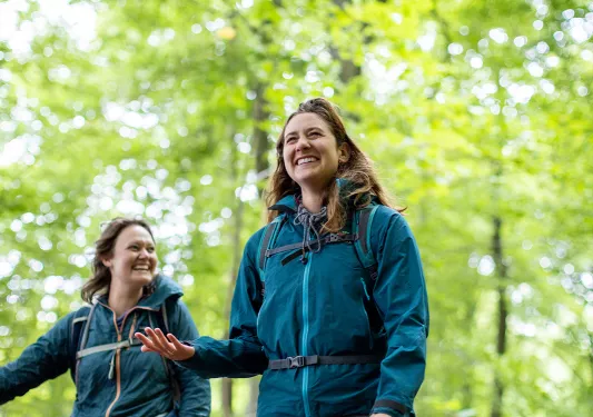 Two women smiling while hiking through a forest