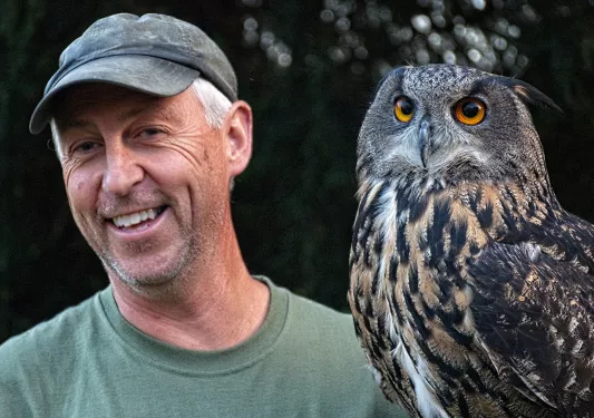 Man wearing a hat smiling next to an owl