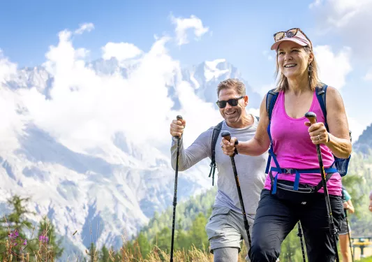 Man and woman with walking poles ascending a grassy mountain