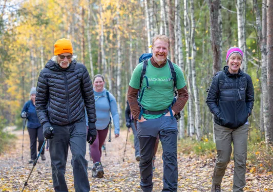 Group of hikers smiling while walking through a dirt trail in a forest