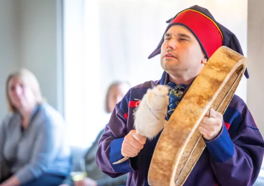 Man in traditional attire playing an instrument with a crowd of people behind him