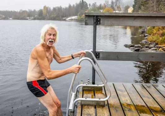 Older man hanging onto railing before jumping into a cold lake