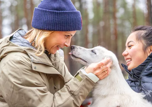 Two women smiling while holding onto a dog