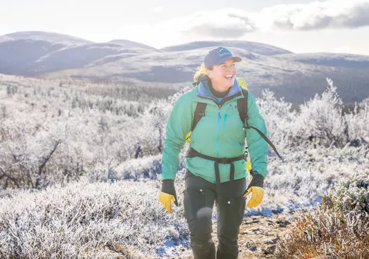Woman in a green jacking, hiking through a snowy valley