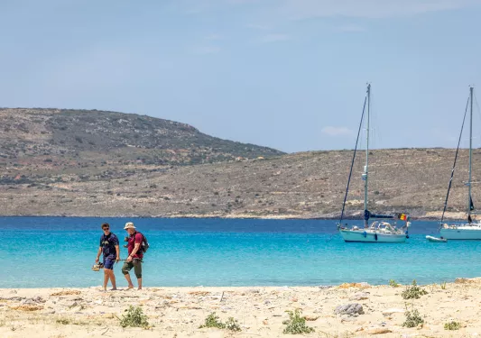 Two people on the beach walking next to the ocean with their shoes in hand