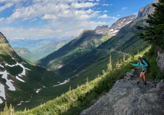 Girl wearing blue, pointing at a large valley and grassy mountains