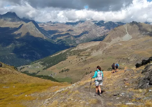 Woman with walking poles descending down a dirt hill covered with rocks