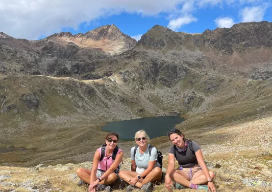 Three women sitting on a hill, with a small lake in the distance