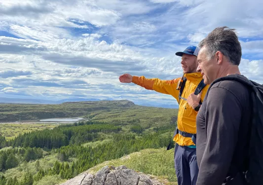 Two men on top of a mountain looking down at a forest of trees