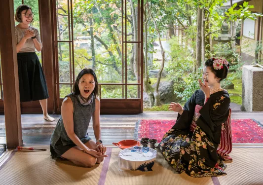 Woman sitting in front of a geisha, kneeling on the ground