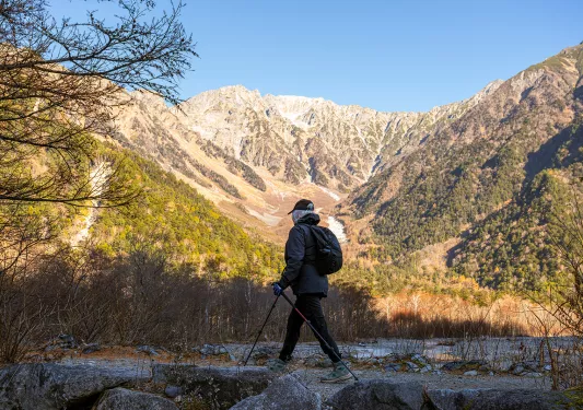 Person with walking poles walking on stone with large mountains in the background