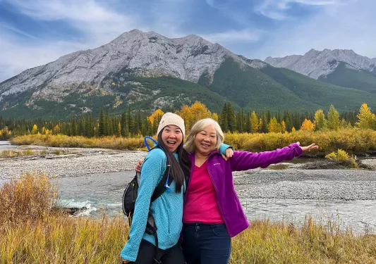 Two woman smiling with their arms open with a mountain in the background