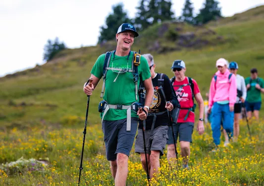 Group of people with walking poles hiking through a valley of grass and yellow flowers