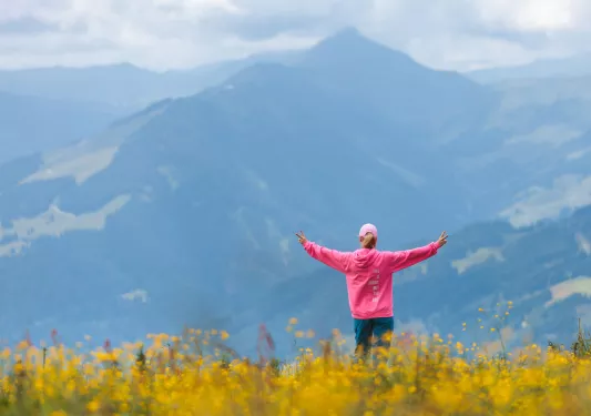 Woman wearing a pink jacket on top of a hill with her arms open