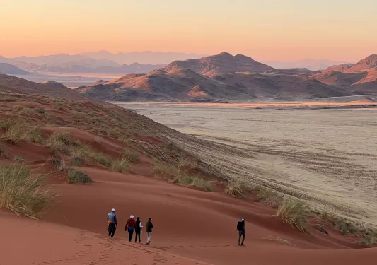 Group of hikers walking down sand dunes towards a valley of white dirt