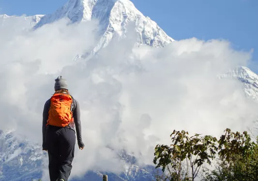 Woman with orange backpack ascending hill towards foggy mountain