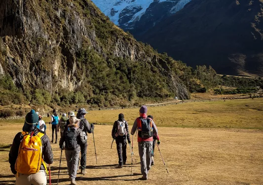 Group of hikers going through a dried field towards mountains
