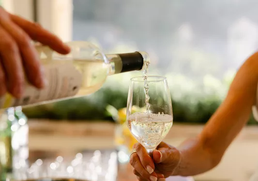 Person pouring wine into a glass being held by another person