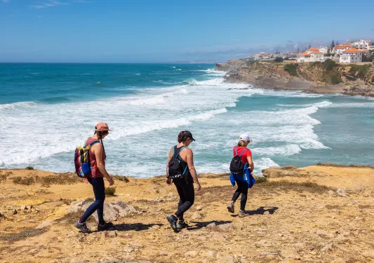 Three women descending down a dirt path towards a beach