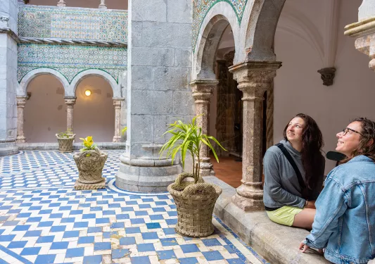 Two women sitting in a castle-like courtyard, looking up to the sky