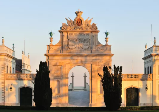 Stone archway with two large bushes in front, with a view of the sunset sky