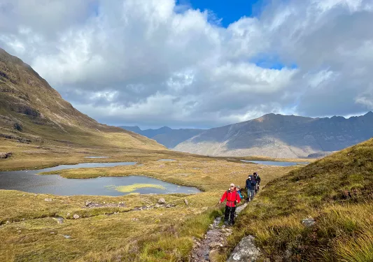 Group of people with walking poles hiking on a gravel trail next to ponds