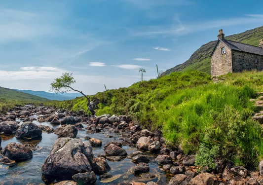 Boulders scattered through a river with a house on top of a small hill