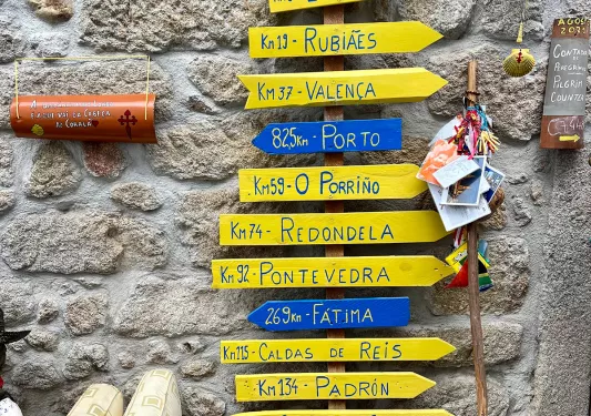 A sign against a stone with with yellow and blue arrows pointing in different directions