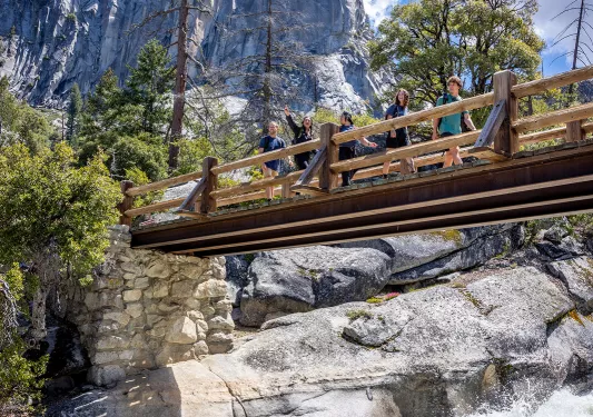 hikers cross a bridge over a roaring waterfall
