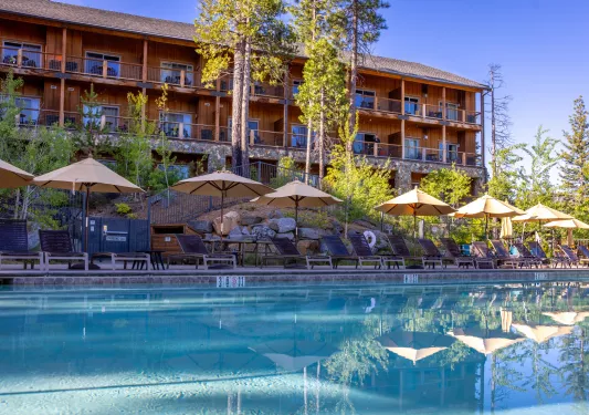 Outdoor pool surrounded by tan umbrellas and a wooden cabin in the background
