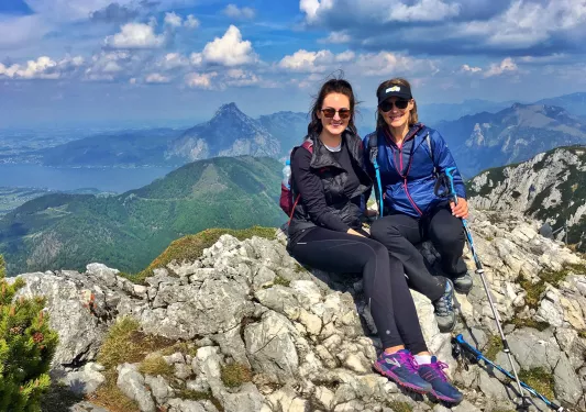 Two women sitting on a pile of rocks at the top of a mountain