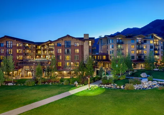 Wide, exterior view of stone hotel buildings with a large grass field in front