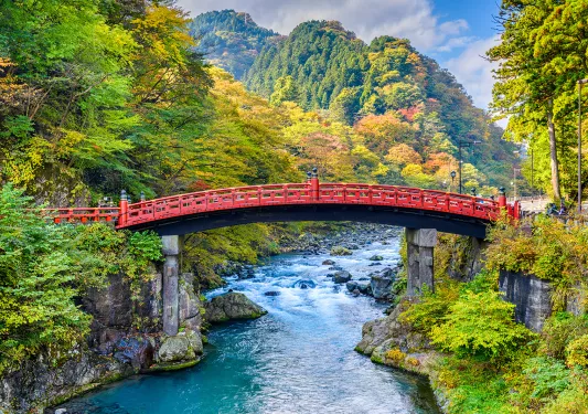 Red bridge over an active river, with large mountains in the background