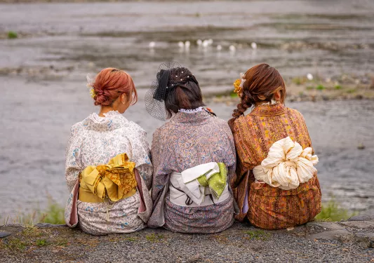 Three women wearing yukatas, sitting on a ledge