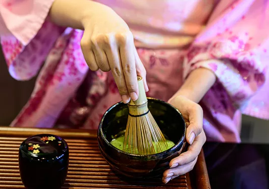 Person making a matcha drink with a whisk and bowl