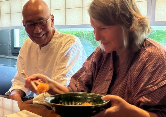 Woman grabbing food with chopsticks, with a smiling man to the left