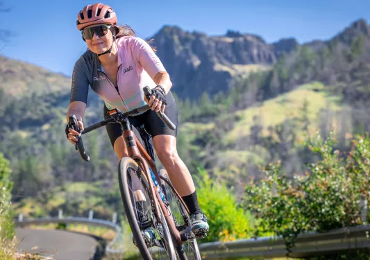 Woman in pink biking gear, riding her bike on an empty road in the hills